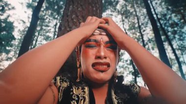 Düşük açılı bir yakın plan, ıstırap içinde çığlık atan bir Java dansçısının saf duygularını yakalar. Bir ağaca yaslanmış, başını güçlü, dramatik bir acı ve umutsuzluk performansıyla kavrıyor..