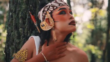 Okçu kostümlü, ağaca yaslanmış bir Java erkek dansçısının yakın çekimi. Dramatik makyajı ve düşünceli ifadesi ormandaki düşünceli, kederli ya da beklenti dolu bir hikayeyi anlatıyor..