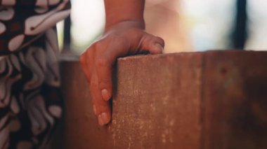 Bir Java dansçısının çıkıntıda dinlenen elinin sessiz ve detaylı bir görüntüsü. Çekimde geleneksel batik kumaş ve yasemin çiçeği çelenkleriyle süslenmiş beyaz bir kuşak yer alıyor (ronce melati)).