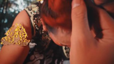 Aşırı yakın çekim, başı dertte olan bir Cava dansçısının çılgınca hareketlerini yakalar. Elleri saçlarını kaotik ve duygusal bir şekilde çekiyor. Delilik, acı ve iç karışıklığın performansı..