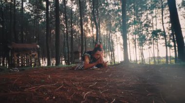 Geleneksel kıyafetli bir Java dansçısı umutsuzca orman zeminine yığıldı. Bu geniş çekim, günbatımının ağaçların arkasında olmasıyla dramatik ve dokunaklı bir keder ve umutsuzluk anını yakalar..