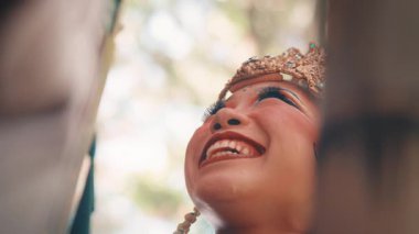 Yaratıcı düşük açılı yakın plan çekimler, dişi bir Java dansçısının gülerken yüzündeki saf mutluluğu yakalar. Süslü altın başlığı ve geleneksel makyajı çok güzel..