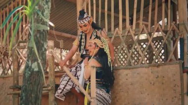 Bambu kulübesinde şakalaşan, klasik bir hikayeden büyüleyici bir Cava çifti sahnesi. Gülüşleri ve jestleri bir flört, aşk ve mutluluk hikayesi anlatıyor..