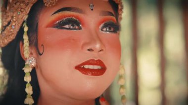 Dişi bir Cava dansçısının göz kamaştırıcı yakın çekimi. Onun sakin ve düşünceli ifadesi dramatik, geleneksel makyajla ve yasemin çiçekleriyle süslenmiş altın başlıkla vurgulanıyor..