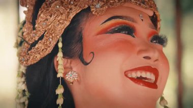 Geleneksel bir Cava dansçısının mutlu yüzüne aşırı yakın çekim. Işıl ışıl gülüşü, karmaşık makyajı ve altın başlığının ve yasemin çiçeklerinin ayrıntıları çok güzel bir şekilde yakalandı..