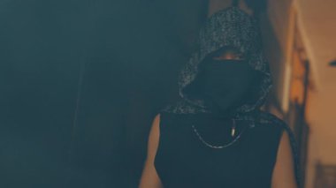 Kapüşonlu ve yüzü örtülü gizemli bir figür loş bir ortamda duruyor. Atmosfer dengesiz ve esrarengiz. Entrika ya da gizlilik gibi..