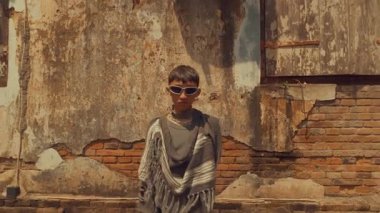 Kıyamet sonrası kostümleri içinde yıpranmış bir duvarın yanından geçen bir grup insan. Sahne, giysilerinde çeşitli doku ve renklerle bir hayatta kalma ve macera hissi taşır..