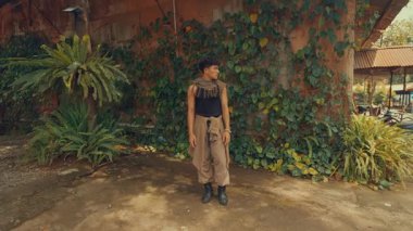 Yeşillik ve sarmaşıklarla çevrili bir yerde dans eden bir dansçı. Dansçı şık bir kıyafet giyer ve dinamik hareketler sergiler. Enerji ve yaratıcılığı somutlaştırır..