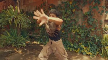 Açık havada break dans yapan bir dansçı çeviklik ve beceri sergiliyor. Arkaplanda yemyeşil bir ortam ve kırsal bir ortam var. Sahneye canlı bir atmosfer katıyor..