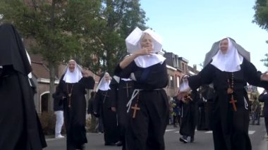 Belçika 'nın Antwerp kentindeki Wilrijk Geitenstoet adlı geleneksel bir fuarda rahibeler gibi el sallayan kadınlar. bandajlı kol