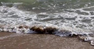 Deniz kıyısını kapatın. Sakin okyanus suyu dalgaları kumlu sahile vuruyor. Küçük deniz dalgaları yavaş çekimde kırılıyor. Soyut doğa arka plan seyahati rahatla