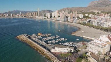 Benidorm marinasının İnsansız Hava Aracı 'ndan Tranquil Aerial View. Sabah ışığında, gökdelenli ve arka planda plajlı statik bir video. Martılar havada uçuyor.