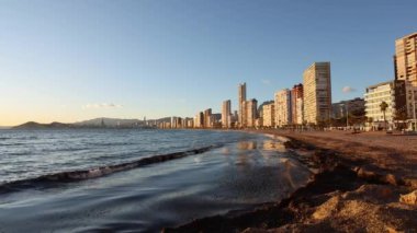 Benidorm plajının yavaş çekim görüntüleri ve arka planda gökdelenler olan dalgalar güzel öğleden sonra altın ışıklarıyla