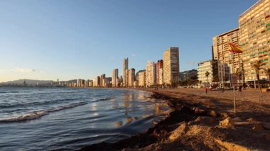 Benidorm plajının durağan videosu altın öğleden sonra ışığında direğin üzerinde İspanyol bayrağı sallıyor.