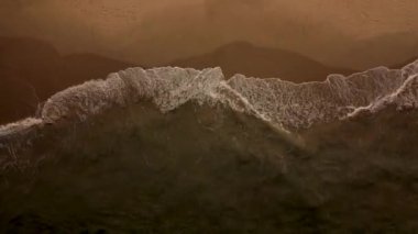 Karanlıkta kumların üzerinde kırılan dalgaların havadan drone görüntüsü.