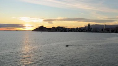 Benidorm ufuk çizgisi ve deniz gün batımında tekne geçiyor.