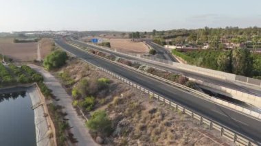 A drone slowly ascends, capturing the bustling AP7 motorway adjacent to lush camping grounds under the warm Torrevieja sun.