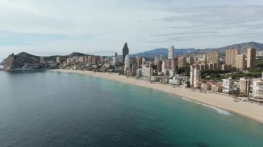 Benidorm kıyı şeridinin havadan görünüşü. Kumlu kumsallar, yüksek gökdelenler ve kıyı boyunca uzanan berrak Akdeniz sularıyla uzak dağlar.
