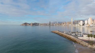 Sabit bir insansız hava aracı Benidorm 'un sahil şeridini bir marinayla, sakin Akdeniz sularıyla ve temiz bir gökyüzünün altında şehrin ufuk çizgisini yakalıyor.