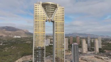 Benidorm 'un Intempo gökdeleninin hava drone görüntüsü, açık bir günde arka planda görünen diğer gökdelenler ve dağlarla birlikte benzersiz mimarisini tepeden tırnağa sergiliyor.