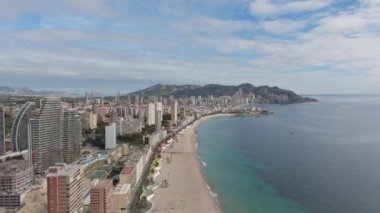 Güneşli bir günde şehrin ufuk çizgisi, kumlu plajları ve berrak Akdeniz sularını gören Benidorm kıyı şeridini görüntüleyen hava statik görüntüsü.
