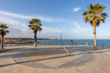 Playa Flamenca, Costa Blanca, İspanya 'nın sahil yolundaki güneş saati ve palmiye ağaçlarının panoramik manzarası..