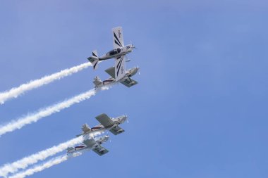 Bir grup akrobatik uçak yakın düzende uçuyor, açık mavi gökyüzü altında hava gösterisi sırasında duman izi bırakıyorlar.