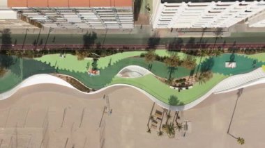 Benidorm 'un hava manzarası İHA yandan hareket ederken bisikletçileri, yayaları ve sahil yolunun dalgalı tasarımını yakalıyor.