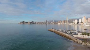 İnsansız hava aracı Benidorm 'un sahil şeridine yükseliyor, sakin Akdeniz sularının üzerinde uçan martıların huzurlu bir görüntüsünü yakalıyor, şehrin ufuk çizgisi ve marinası görüş alanımızda.