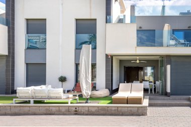 İçinde şezlonglar, rahat bir oturma alanı ve gösterişli tasarım öğeleri bulunan modern bir açık hava verandası, konut kompleksi içinde rahatlama ve rahatlama alanı sunuyor.