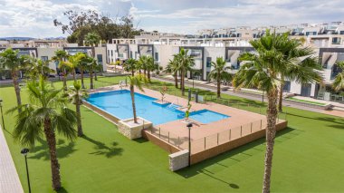 Palmiye ağaçları ve yeşil çimlerle çevrili büyük bir havuzu olan lüks bir apartman kompleksi, sakinleri için rahatlatıcı bir açık hava ortamı sunuyor.
