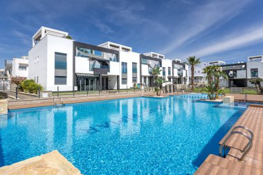  Geniş bir yüzme havuzu, palmiye ağaçları ve yeşil alanlar içeren modern yerleşim alanı, rahatlatıcı bir açık hava ortamı yaratıyor.