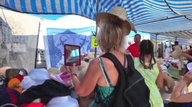  Bir kadın, Torrevieja 'da çeşitli şapka ve aksesuarlarla çevrili bir markette güneş şapkasını denemek için el aynası kullanıyor.