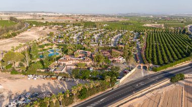 İspanya 'nın Torrevieja kentindeki AP-7 otoyolunun yakınındaki yemyeşil tarım arazisiyle çevrili bir tatil beldesinin havadan görüntüsü, sabah ışığında çekildi.