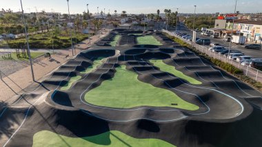 Torrevieja Spain 20 October 2024:  A detailed view of the pump track in El Chaparral, Torrevieja, highlighting smooth asphalt curves, vibrant green patterns, and nearby urban and natural spaces clipart