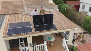 Torrevieja 'da kırmızı kiremitli bir villanın çatısına güneş panelleri kuran bir işçinin yakın görüntüsü, sürdürülebilir enerji çözümlerini teşvik ediyor.