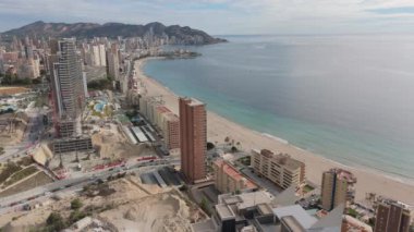 Benidorm 'un sahil manzarası, kumlu sahil ve sakin Akdeniz sularının kıyı şeridi boyunca uzandığı modern gökdelenler ve devam eden inşaatın bir karışımını vurguluyor..