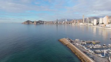 Benidorm 'un sahil manzarası, kumlu sahil ve sakin Akdeniz sularının kıyı şeridi boyunca uzandığı modern gökdelenler ve devam eden inşaatın bir karışımını vurguluyor..