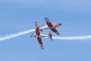 İki Patrouille Suisse uçağı, hava gösterisi sırasında, açık mavi gökyüzüne karşı hassas bir uçuş gerçekleştirerek, duman izleriyle çarpıcı bir geçiş manevrası gerçekleştiriyor..