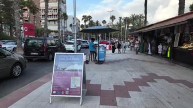 Torrevieja 'nın kalabalık caddesinde, arka planda dükkanları, arabaları ve yayaları olan Las Salinas' a bir turist treninin tanıtımını yapan bir tabela bulunuyor..