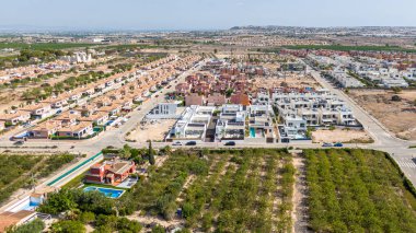 İspanya 'nın Torrevieja şehrinde güneşli bir gökyüzünün altında konut, modern konut ve çevreleyen yeşil alanlar gösteren hava görüntüleri.