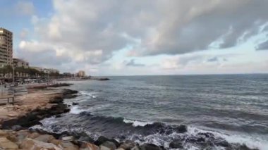 Torrevieja 'da sakin bir sahil manzarası. Kayalık bir kıyı şeridi, yumuşak dalgalar ve bulutlu bir gökyüzünün altındaki şehir manzarası..