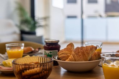 Bir kase kruvasan, portakal suyu, reçel ve bisküvi içeren rahat bir kahvaltı masası..