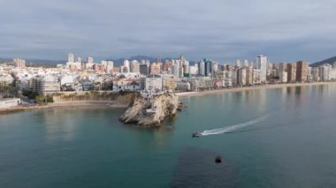 Benidorm 'un kıyı şeridinde sakin sularda yüzen ikonik Balkon del Mediterraneo' nun havadan görüntüsü ve şehrin ufuk çizgisi dağlık bir zemin üzerine kurulmuş..