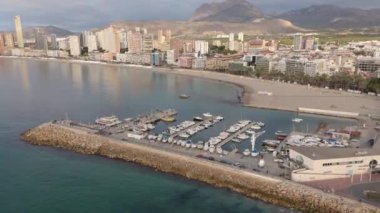 Benidorm 'un marinasının kumlu Levante Sahili sahil şeridine yakın rıhtımında kentin gökdelenleri ve dağlarının zeminine sahip tekneleri olan havadan görüntüsü..
