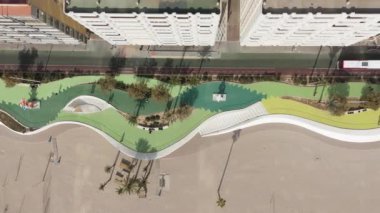 Benidorm 'daki yeni sahil şeridinin tepeden aşağı hava manzarası, dalgalı tasarımı, bitişik binalar ve kumlu plajlar, güneşli bir günde gölgeler bırakan palmiye ağaçları..