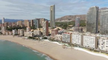 Benidorm sahilinin ikonik Intempo Kulesi ve modern gökdelenleri çevreleyen hava manzarası. Sakin Akdeniz görünür.