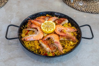 Karides, balık ve taze limon dilimleriyle süslenmiş dökme demir bir tavada servis edilen geleneksel deniz ürünleri paellasının yukarıdan görünüşü. İspanyol mutfağı en iyisidir..