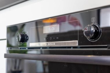 Modern bir mutfakta dijital ekran ve kontrol düğmeleri olan parlak siyah bir Bosch fırınının detaylı görüntüsü.