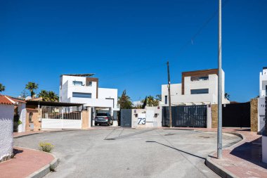 Güvenli kapıları, palmiyeleri ve mavi gökyüzü olan sessiz bir sokağın sonundaki modern beyaz villaların sokak manzarası..